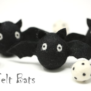 May include: Black felt bats with white eyes and wings are displayed with white balls with black spots. The text "Felt Bats" is below the bats. These Halloween decorations are perfect for a spooky holiday.