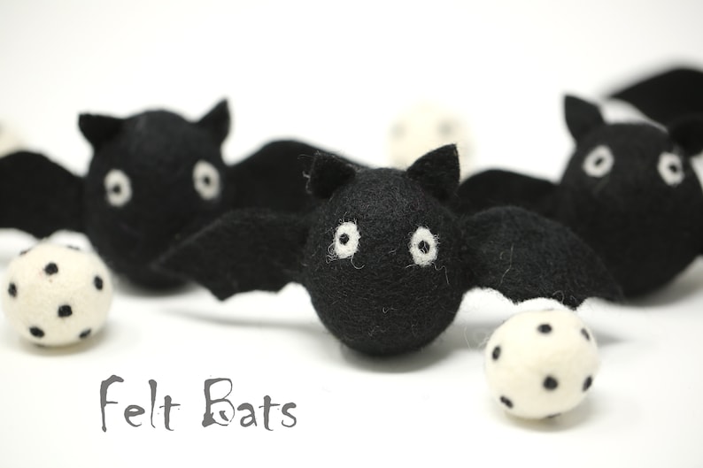 May include: Black felt bats with white eyes and wings are displayed with white balls with black spots. The text "Felt Bats" is below the bats. These Halloween decorations are perfect for a spooky holiday.