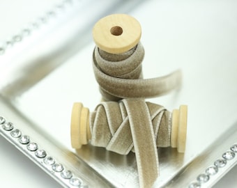 May include: Two spools of beige velvet ribbon with a satin edge. The ribbon is wrapped around wooden spools.