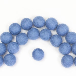 Könnte beinhalten: Eine Sammlung von 18 blauen Filzkugeln, die in einem Bogen angeordnet sind, mit einer Kugel in der Mitte. Die Kugeln sind alle gleich groß und aus einem weichen, flauschigen Material gefertigt.