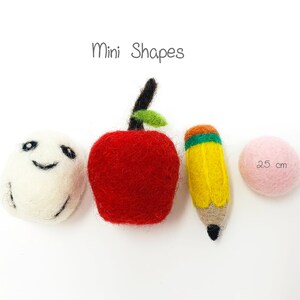 May include: Mini felt shapes, including a red apple, a yellow pencil, a white ball with a smiley face, and a pink ball. The text "Mini Shapes" is above the shapes. The pink ball has the text "2.5 cm" on it.