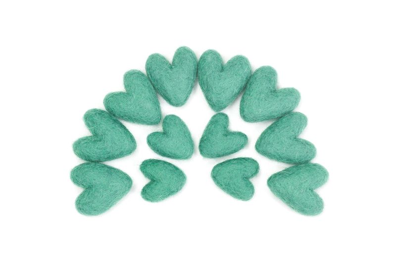 Puede incluir: Un semic&iacute;rculo de corazones de fieltro color turquesa dispuestos en fila. Los corazones son todos del mismo tama&ntilde;o y forma.