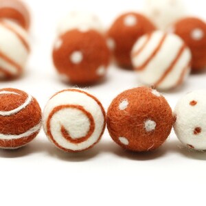Peut inclure: Une collection de boules en feutre marron et blanc avec différents motifs, notamment des rayures, des pois et des volutes.