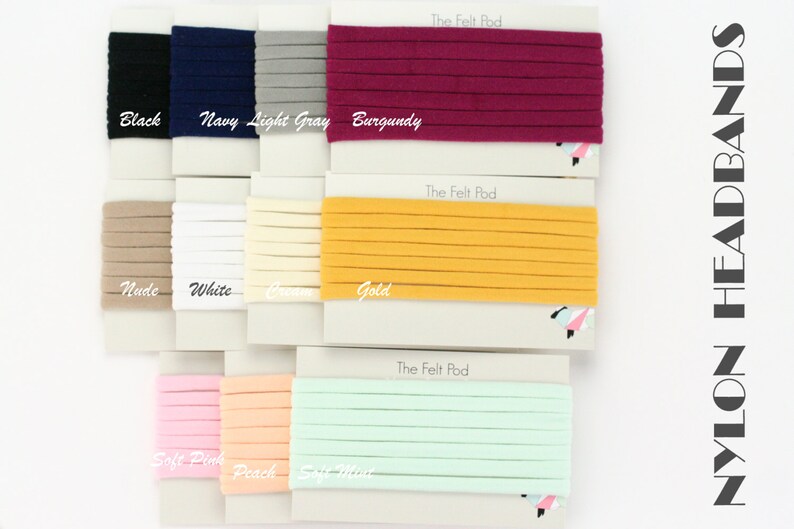 May include: A variety of nylon headbands in different colors, including black, navy, light gray, burgundy, nude, white, cream, gold, soft pink, peach, and soft mint. The headbands are displayed on white cards with the text "The Felt Pod" printed on them. The text "NYLON HEADBANDS" is printed on the right side of the image.
