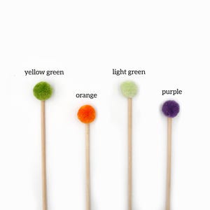 Op de afbeelding: Vijf houten stokjes met pompoenen aan de bovenkant. De pompoenen zijn in de kleuren geelgroen, lichtgroen, oranje, paars.