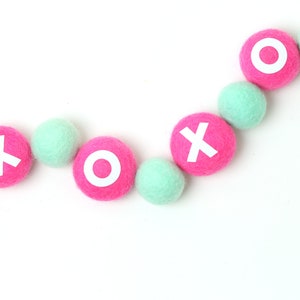 May include: A garland of pink and mint green felt balls with white letters spelling out "XOXO".