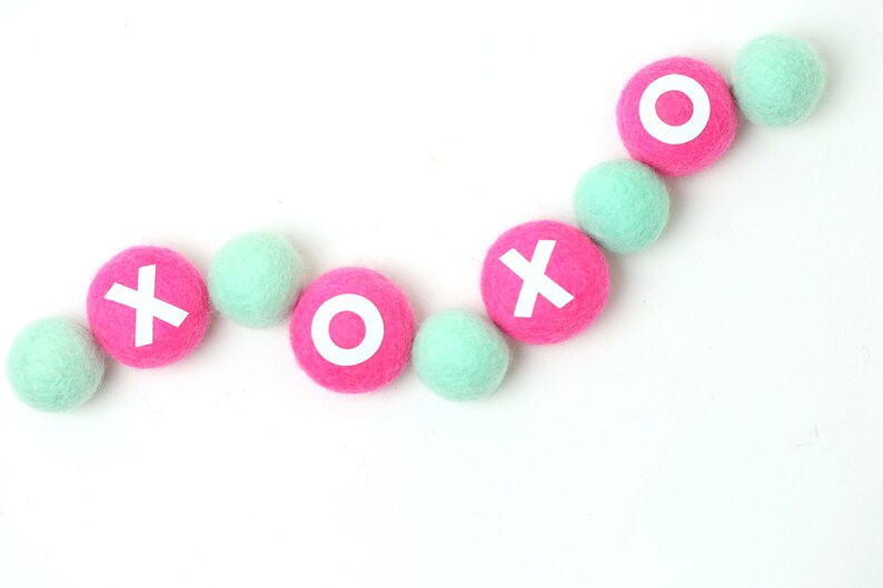 May include: A garland of pink and mint green felt balls with white letters spelling out "XOXO".