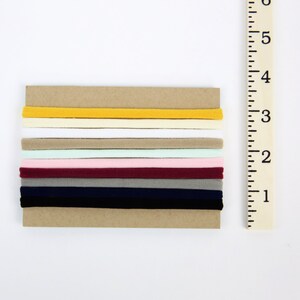 May include: A set of 10 hair ties in various colors, including yellow, white, beige, pink, burgundy, gray, and navy blue. The hair ties are arranged in a stack on a brown background.