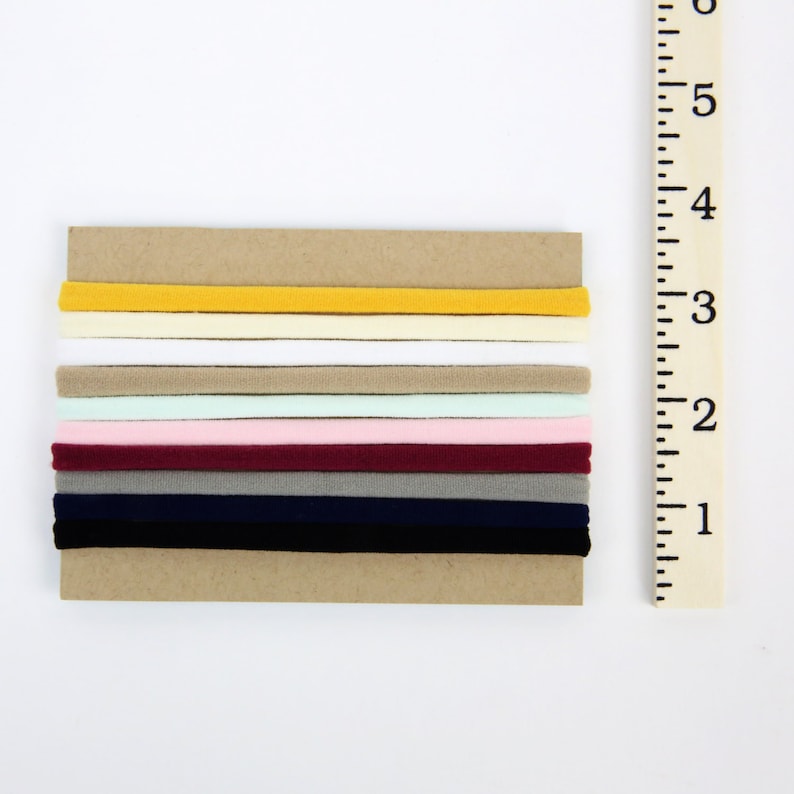 May include: A set of 10 hair ties in various colors, including yellow, white, beige, pink, burgundy, gray, and navy blue. The hair ties are arranged in a stack on a brown background.