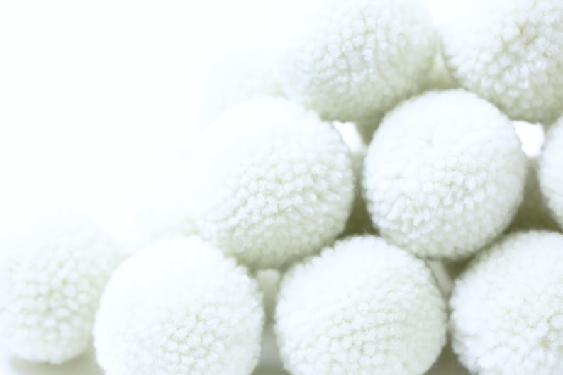 May include: A group of white fluffy pom poms arranged in a pyramid shape. The pom poms are soft and textured, and they are all the same size.