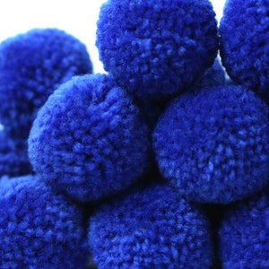 Puede incluir: Un grupo de pompones azules, un tipo de bola de lana esponjosa, están apilados juntos. Los pompones son suaves y peludos, y todos son del mismo tamaño.