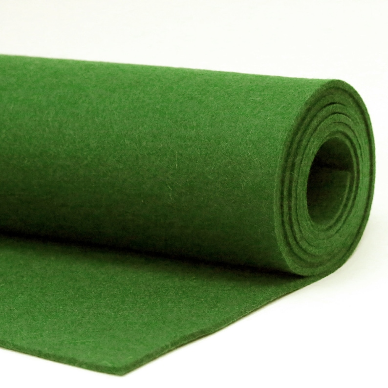 May include: A roll of green felt fabric. The felt is a solid, vibrant green color and appears to be soft and pliable. The roll is partially unrolled, revealing the texture and thickness of the material. The background is plain white.