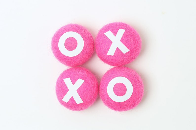 May include: Four pink felt balls with white letters spelling out "XOXO" on a white background.