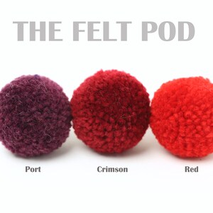 May include: Three felt balls in different shades of red: port, crimson, and red. The felt balls are arranged in a row from left to right.