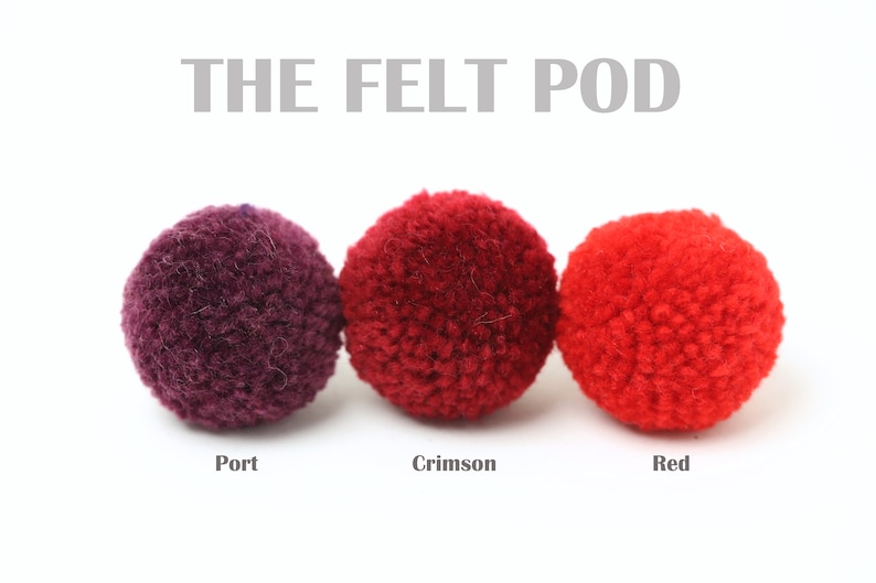 May include: Three felt balls in different shades of red: port, crimson, and red. The felt balls are arranged in a row from left to right.