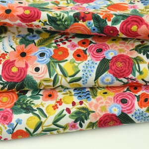 May include: Folded fabric with a colourful floral design. The pattern showcases red, pink, orange, blue, and yellow flowers on a cream backdrop. Green leaves and stems are also visible, creating a botanical theme.