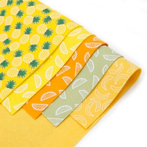 May include: A set of six yellow felt sheets with different fruit patterns. The patterns include pineapples, lemons, limes, and bananas.