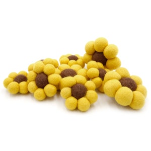 Op de afbeelding: Een groep viltzonnebloemdecoraties in geel en bruin. De bloemen zijn gemaakt van kleine viltballen.