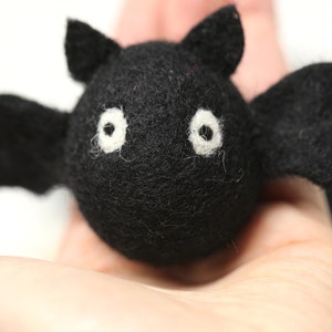 May include: A handmade black felt bat with white eyes and outstretched wings. The bat has a round body and small, pointed ears. This Halloween decoration is perfect for adding a spooky touch to any space.