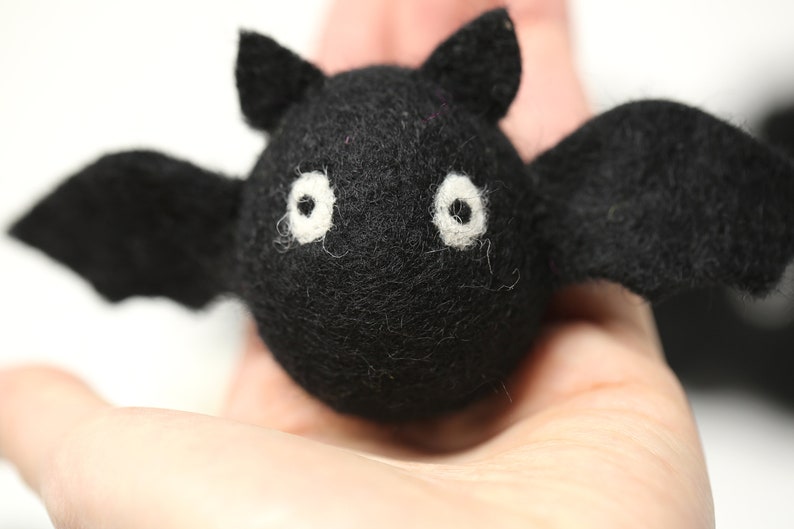May include: A handmade black felt bat with white eyes and outstretched wings. The bat has a round body and small, pointed ears. This Halloween decoration is perfect for adding a spooky touch to any space.