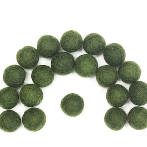 Puede incluir: Una colección de bolas de fieltro verde dispuestas en forma de semicírculo. Las bolas son todas del mismo tamaño y de un color verde oscuro.