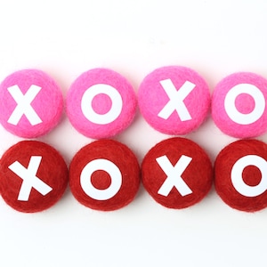 May include: Eight felt balls, four pink and four red, with white letters spelling out "XOXO" in a repeating pattern.