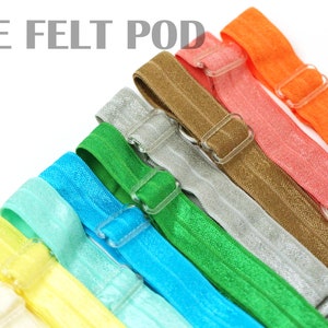 May include: A set of ten colorful elastic hair ties with plastic adjustable buckles. The hair ties are arranged in a rainbow pattern, starting with white, yellow, light blue, turquoise, green, silver, brown, coral, and orange.