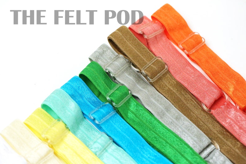 May include: A set of ten colorful elastic hair ties with plastic adjustable buckles. The hair ties are arranged in a rainbow pattern, starting with white, yellow, light blue, turquoise, green, silver, brown, coral, and orange.