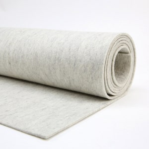 May include: A roll of light gray felt fabric, partially unrolled, showing a textured surface. The felt is a solid color with subtle variations, and the edges are neatly cut. The fabric is suitable for various craft projects.