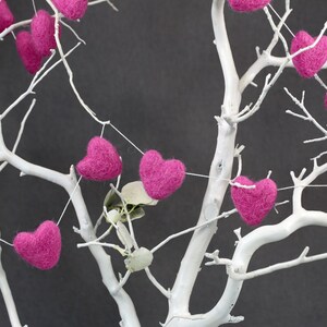 Puede incluir: Un &aacute;rbol de ramas blancas decorado con una guirnalda de corazones de fieltro rosa.