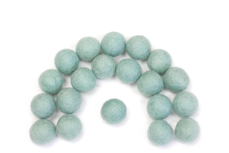 May include: A collection of 20 light blue felt balls arranged in a semi-circle shape.