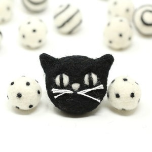 May include: Black felt cat face with white eyes and whiskers, surrounded by white felt balls with black polka dots and stripes.