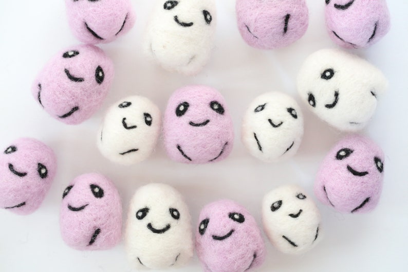 May include: A collection of 14 felt ghost ornaments in pink and white with various facial expressions. The ghosts are all approximately the same size and are arranged in a random pattern on a white background.