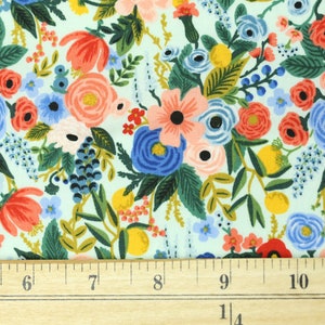 May include: Floral fabric with a pale blue backdrop. The fabric is densely patterned with flowers in red, pink, blue, yellow, and green. A wooden ruler with inch markings is at the bottom.