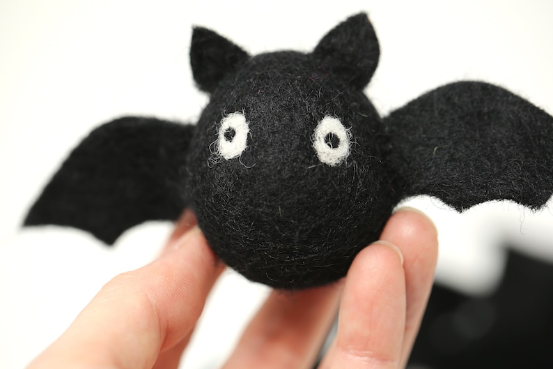 May include: A handmade black felt bat with white eyes and outstretched wings. The bat has a round body and small ears. This Halloween decoration is perfect for adding a spooky touch to any space.