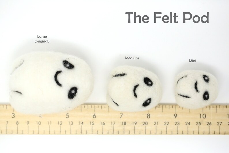 May include: Three felt pods of varying sizes, labeled "Large (original)", "Medium", and "Mini". Each pod is white with a black smiling face and is measured against a wooden ruler.
