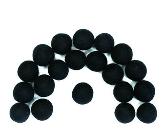 May include: A collection of 18 black felt balls arranged in a semi-circle shape with one ball in the center.