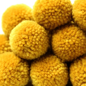 May include: A group of yellow pom-poms, made of yarn, are arranged in a pile. The pom-poms are soft and fluffy.