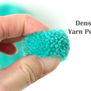 Pu&ograve; includere: Una mano tiene un pompon di lana color turchese brillante. Il pompon &egrave; molto denso e soffice. Il testo "Dense Yarn Pom Poms" &egrave; visibile nell'immagine.