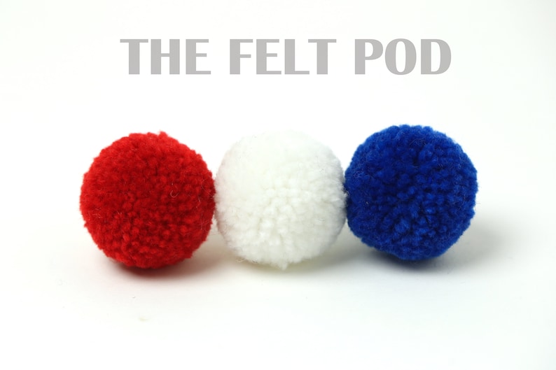 May include: Three felt balls in red, white, and blue colours. The felt balls are arranged in a row from left to right. The text "THE FELT POD" is above the balls.