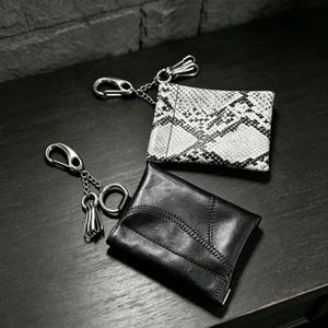 May include: Two rectangular card holders with silver-toned metal keychains attached. One holder features a black and white snakeskin pattern, while the other is solid black with visible stitched seams and a small metal tassel attachment.