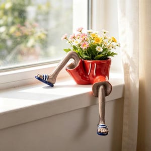 May include: A ceramic planter shaped like a pair of legs wearing red shorts with white drawstrings and blue and white striped sandals. The planter is filled with a bouquet of small pink, yellow, and white daisy-like flowers with green stems.