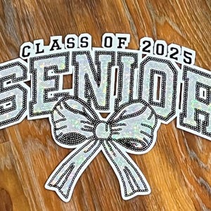 May include: A silver glitter 'Senior' banner with a large bow in the center. The banner also includes the text 'Class of 2025'.