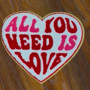 May include: A white heart-shaped rug with a gold border. The words "All You Need Is Love" are written in red and pink fuzzy letters.