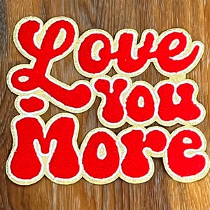 May include: Red felt patch with gold outline, reading "Love You More" in a retro, bubbly font.