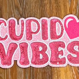May include: Pink and white sequined patch with the text "CUPID VIBES" and a pink heart.