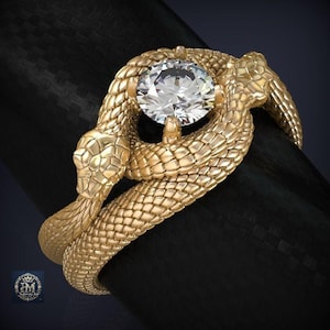 Peut inclure: Une bague en or représentant un serpent enroulé aux écailles texturées entourant une pierre précieuse transparente centrale de taille brillant ronde. La tête du serpent est placée à l'avant et le corps forme l'anneau de la bague.