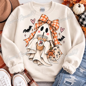Op de afbeelding: Een crèmekleurige sweater met ronde hals en een afbeelding van een geest met een grote oranje-witte geruite strik. De geest houdt een ijskoffiebeker met het label TBREW vast en een klein tasje met een pompoenbedel, omringd door vleermuizen en hartjes.