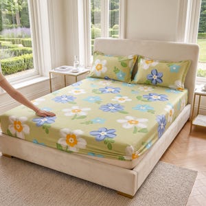 Op de afbeelding: Een beddengoedset met een lichtgroene achtergrond en een herhalend patroon van witte, blauwe en gele bloemen. De set bevat een hoeslaken en twee bijpassende kussenslopen, allemaal voorzien van hetzelfde bloemenprintontwerp.