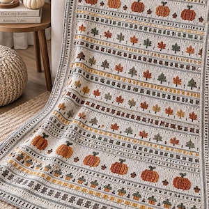 Può includere: Una coperta all'uncinetto con un motivo ripetuto di zucche arancioni, ghiande marroni e verdi e varie foglie autunnali nelle tonalità dell'arancione, giallo e verde. Il design presenta strisce orizzontali testurizzate nei toni crema e grigio.